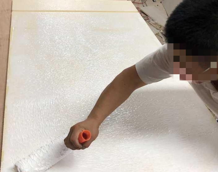工人用滚筒在白色防撞软包板面滚涂胶粘剂,软包墙面安装施工现场实景
